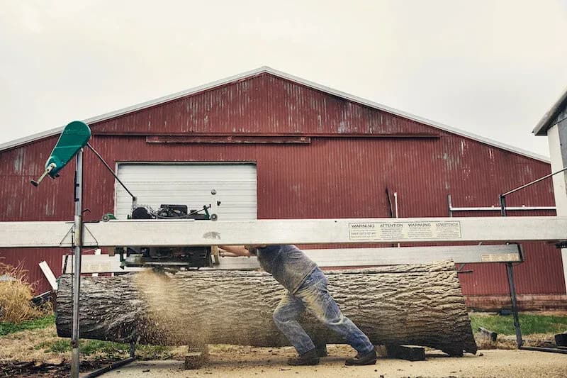 Milling a log beside a red barn