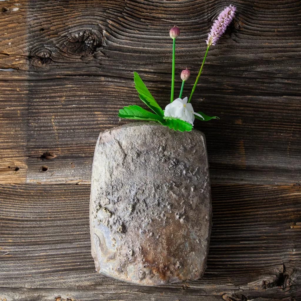 Stoneware wall vase with a spray of flowers, on weathered wood